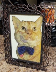 a detailed cross stitch of an orange cat in a blue bowtie